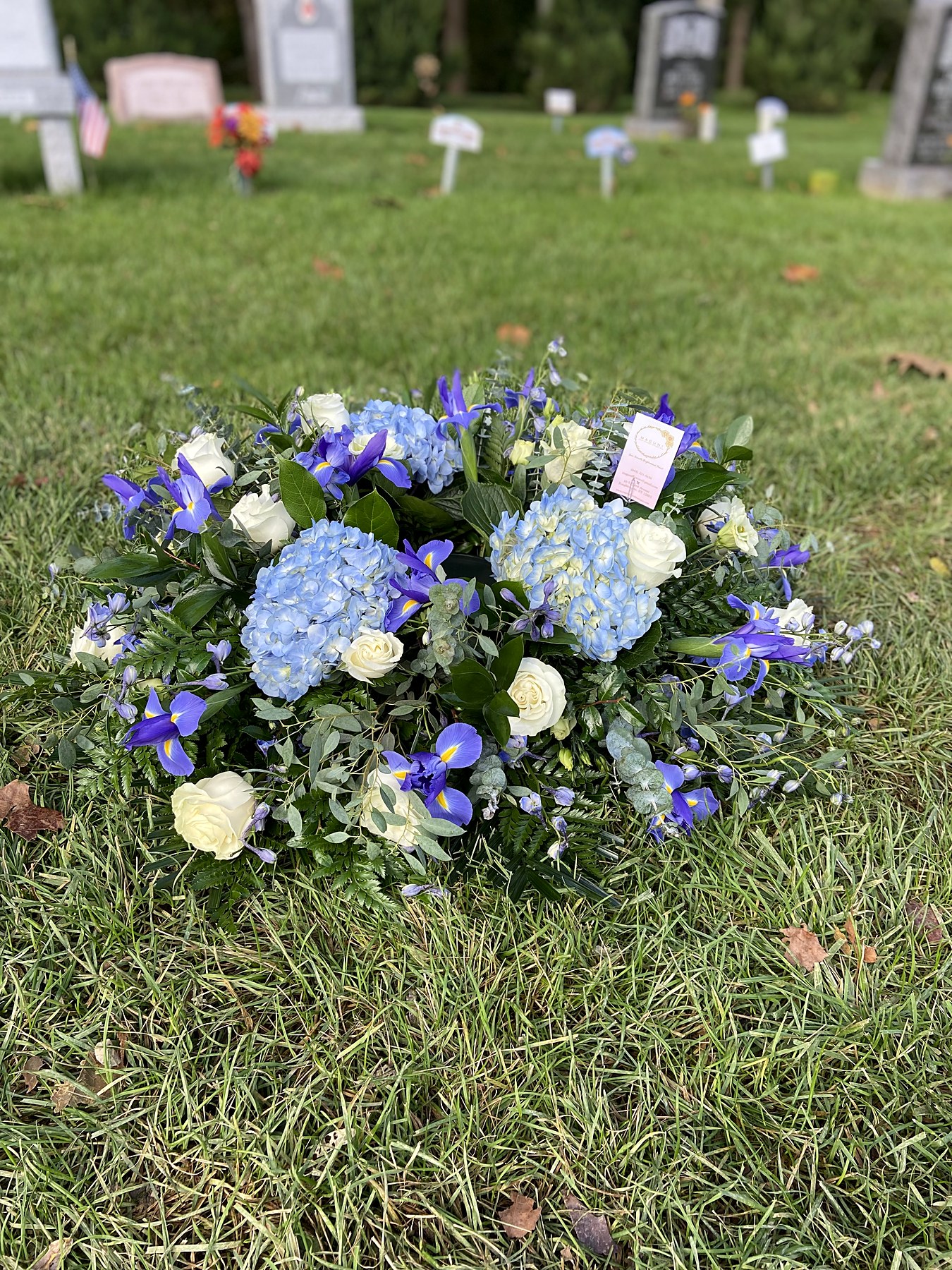 Blue and white graveside spray with hydrangea and roses, set at a cemetery service