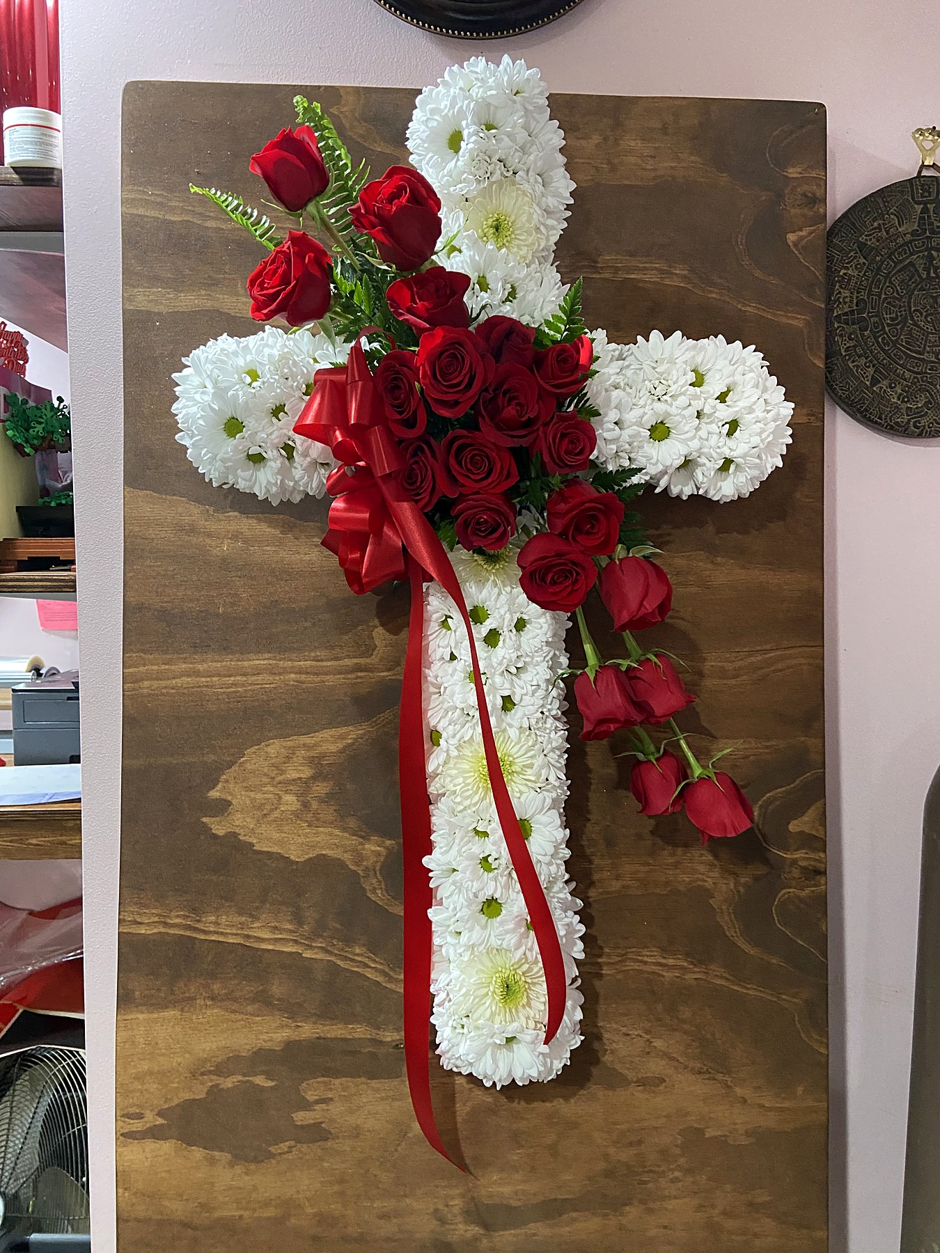 Cross-shaped tribute of white chrysanthemums with red roses and a trailing ribbon