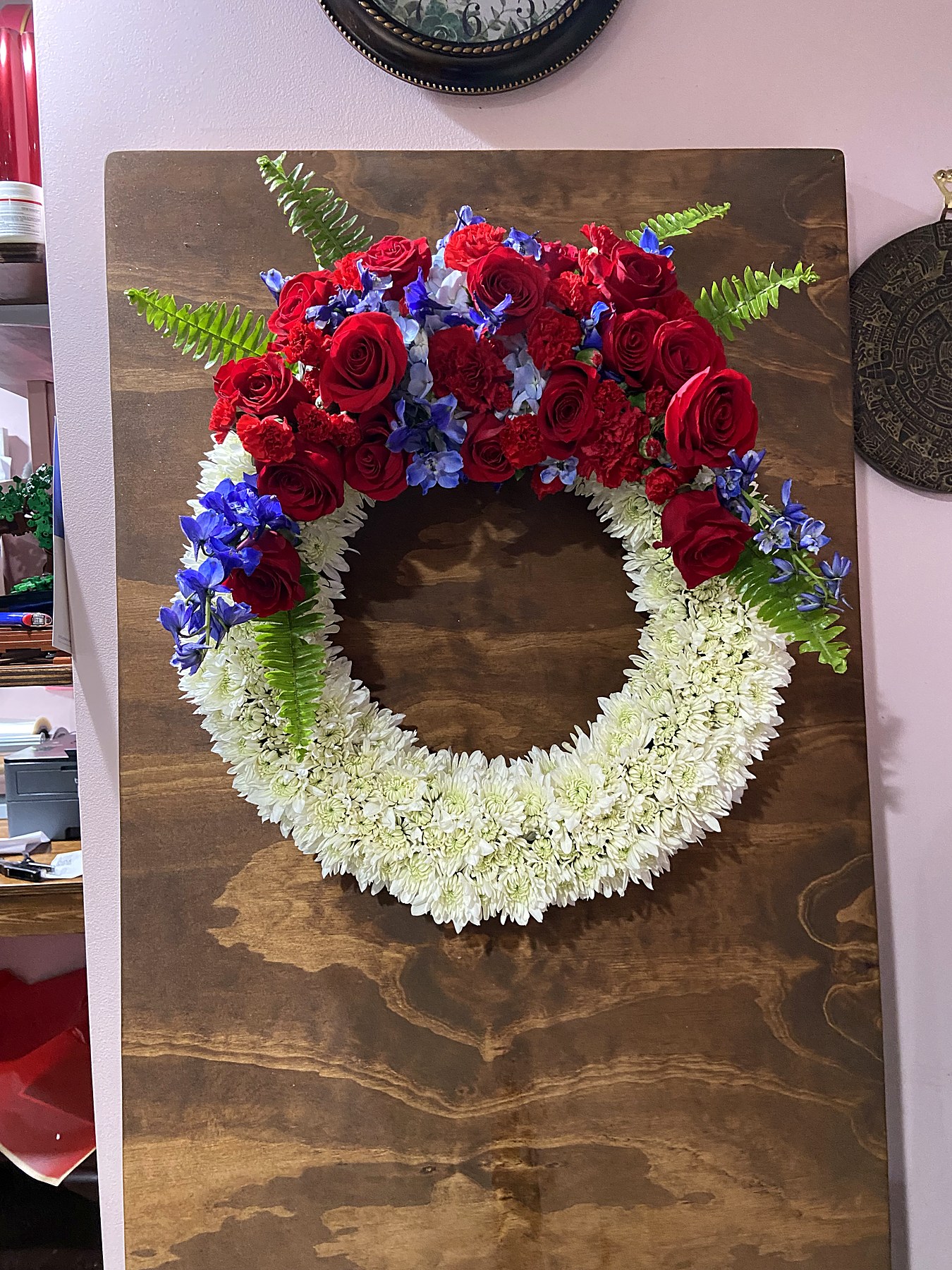 Memorial wreath of white chrysanthemums with red roses, red carnations, and blue delphinium
