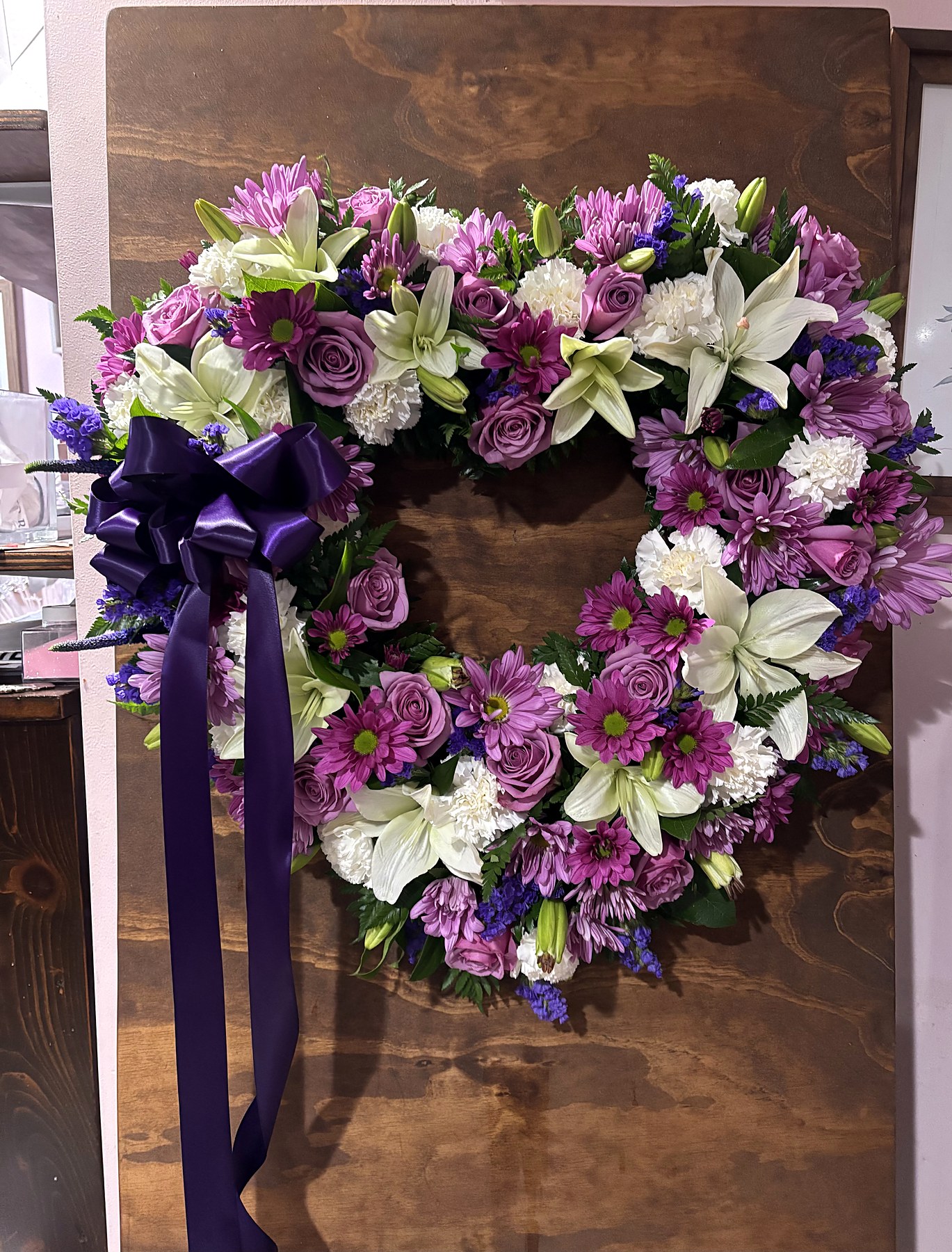 Heart-shaped tribute of purple and white flowers with a purple ribbon